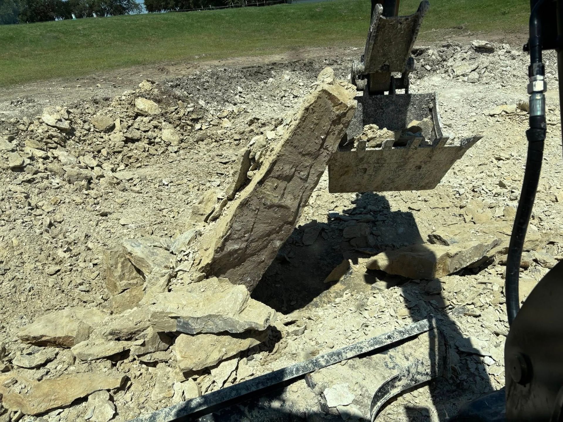 An excavator breaks up concrete, surrounded by debris, outdoors.