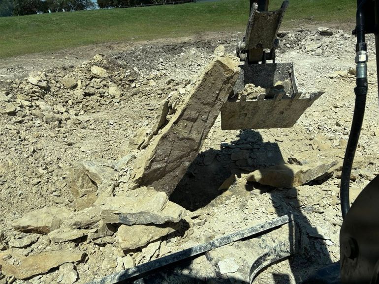 An excavator breaks up concrete, surrounded by debris, outdoors.