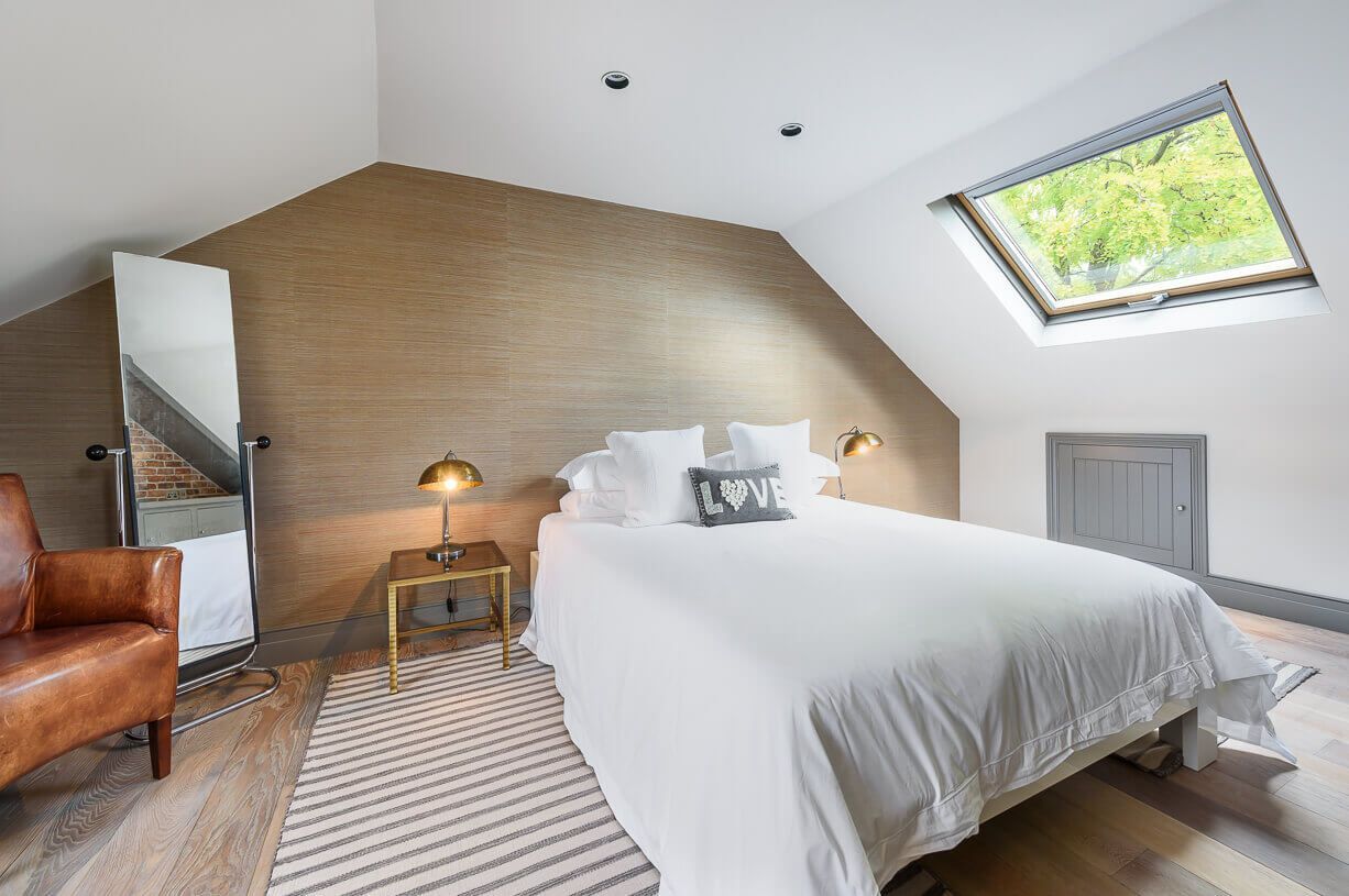 A bedroom with a bed , chair , mirror and skylight.