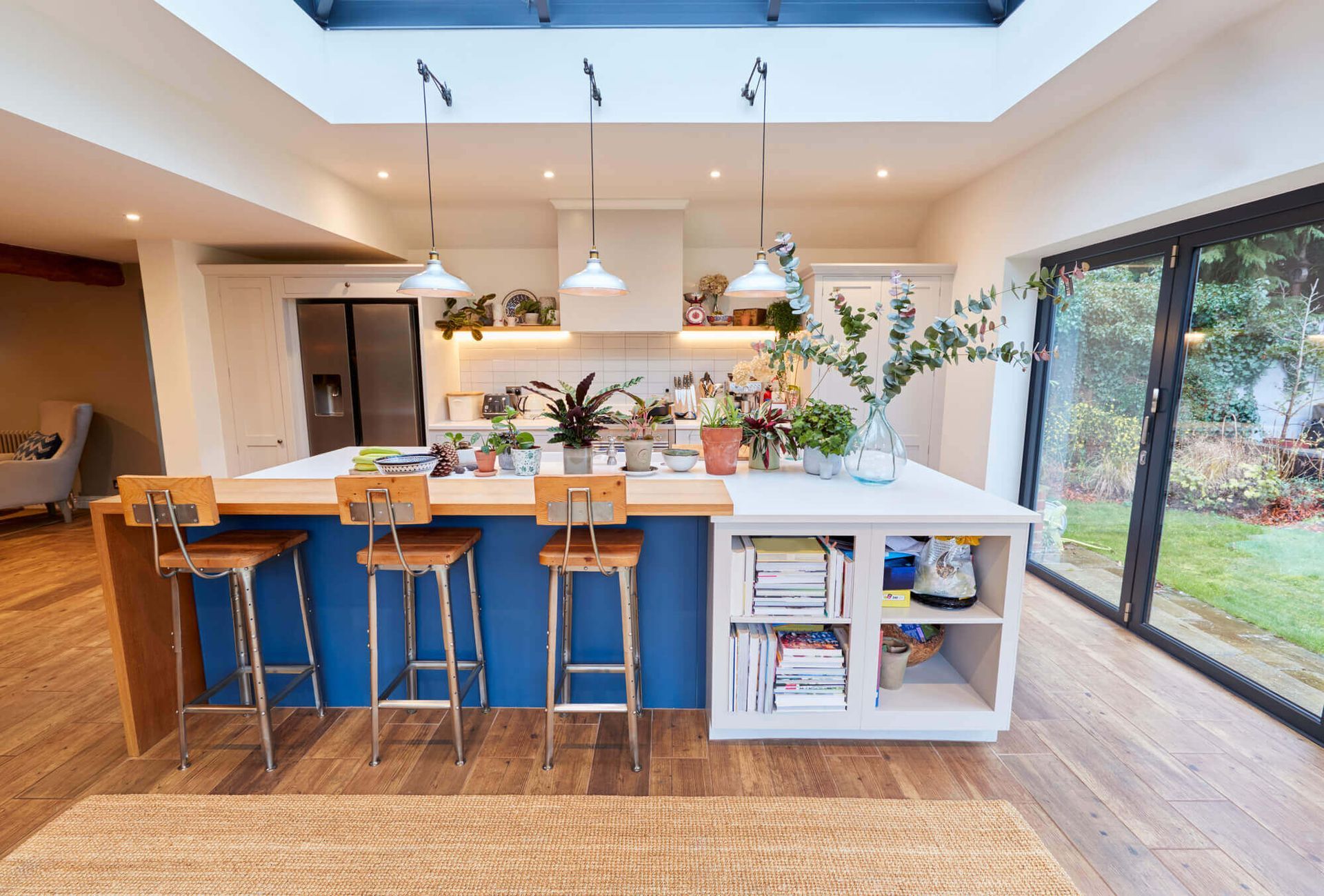 A kitchen with a blue island , stools , a refrigerator and a skylight.