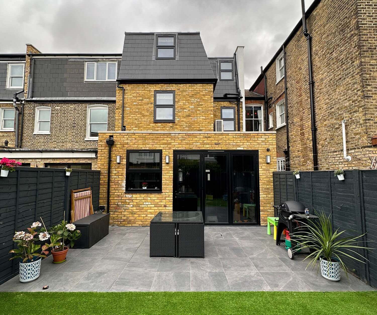 The back of a brick house with a patio area in front of it.