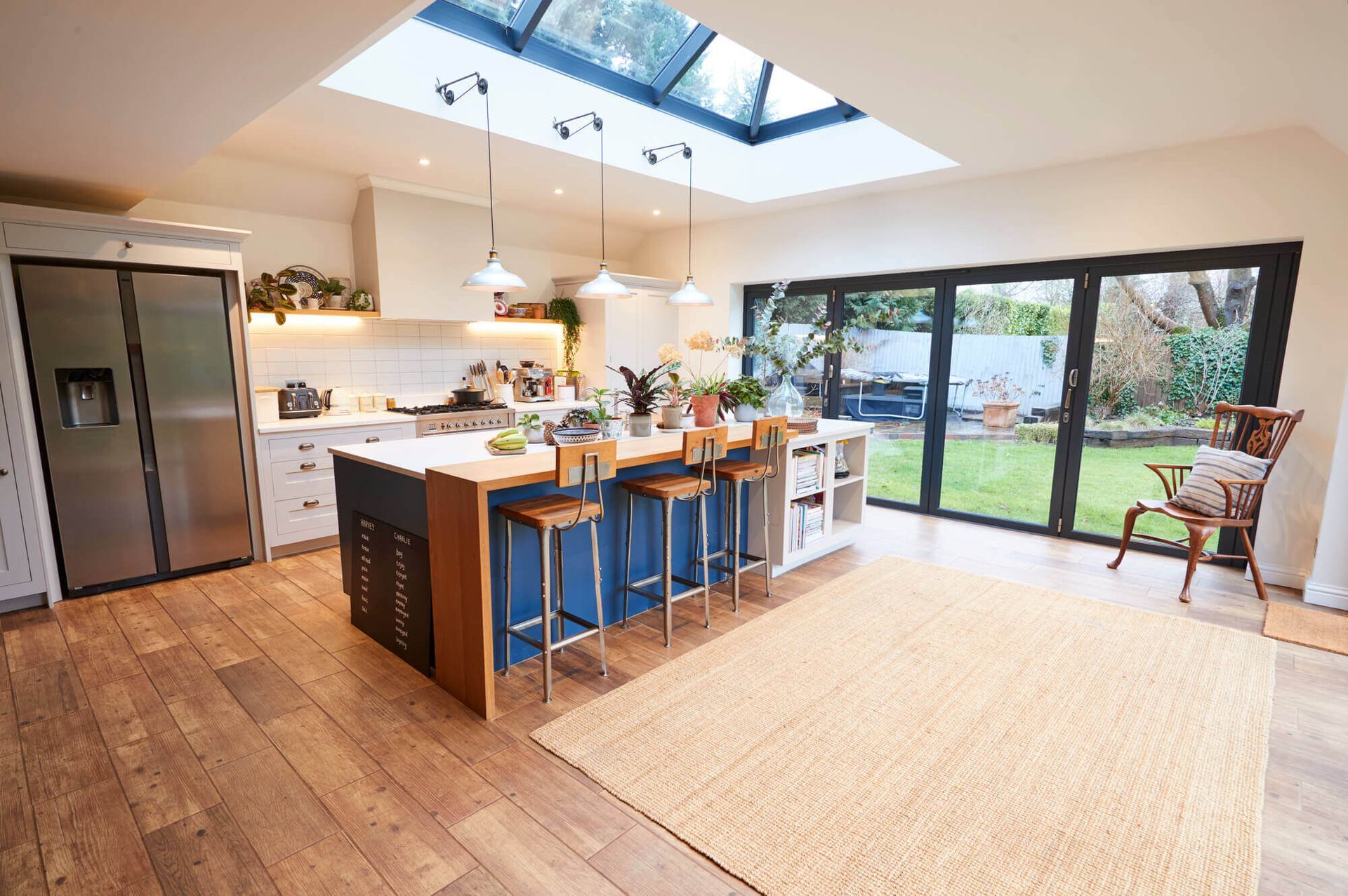 A kitchen with a large island , stools , a refrigerator and a skylight.