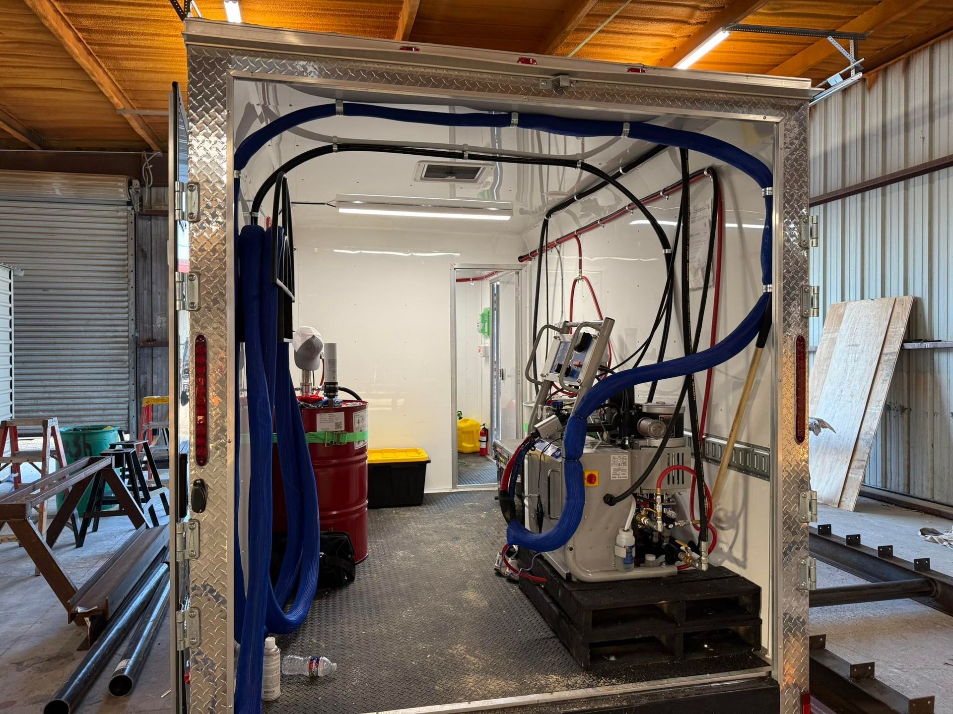 Interior of a utility trailer with equipment, including hoses, a machine, and a fire extinguisher.