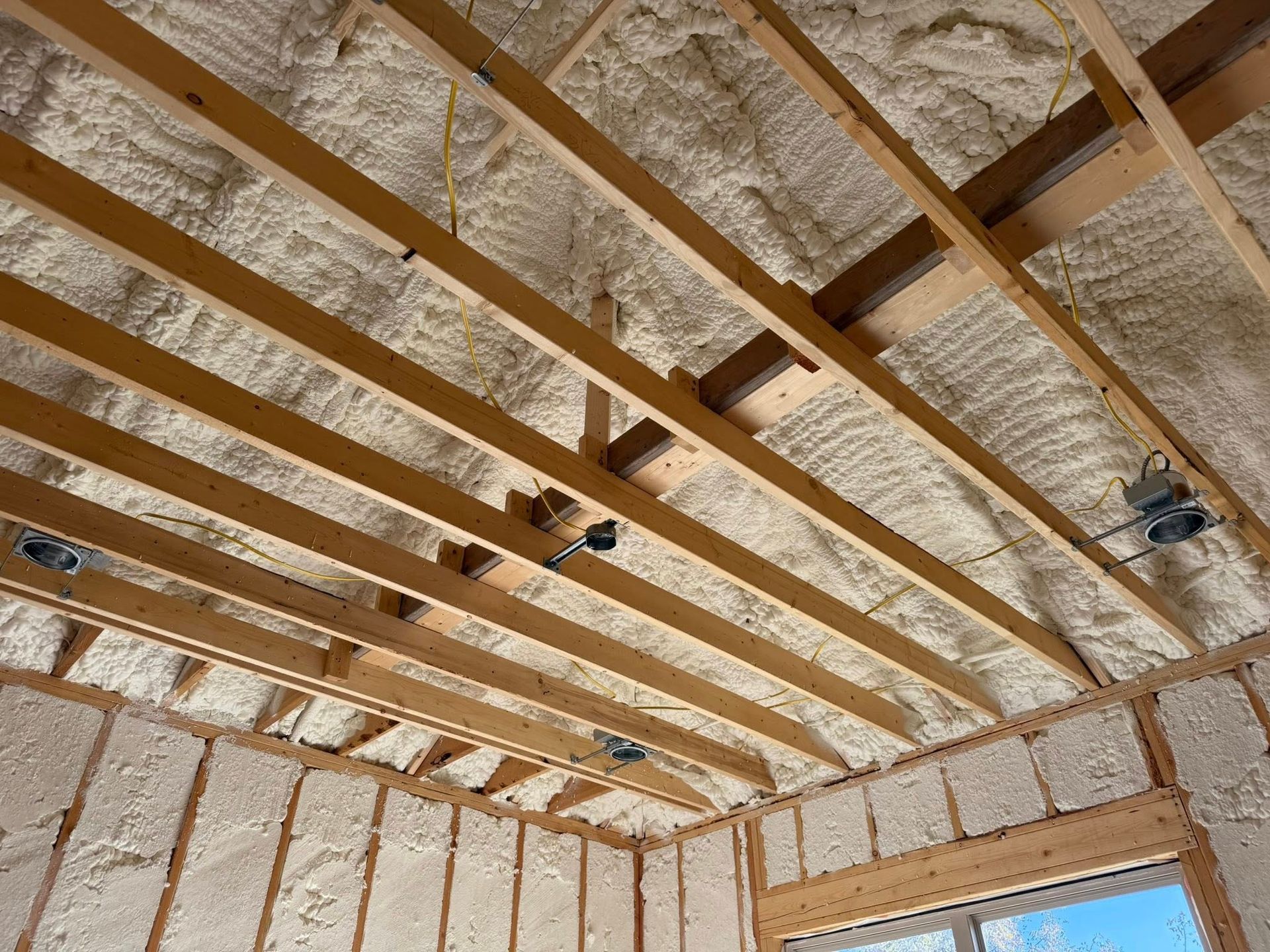 Interior view of a building's unfinished ceiling and walls, insulated with sprayed foam.