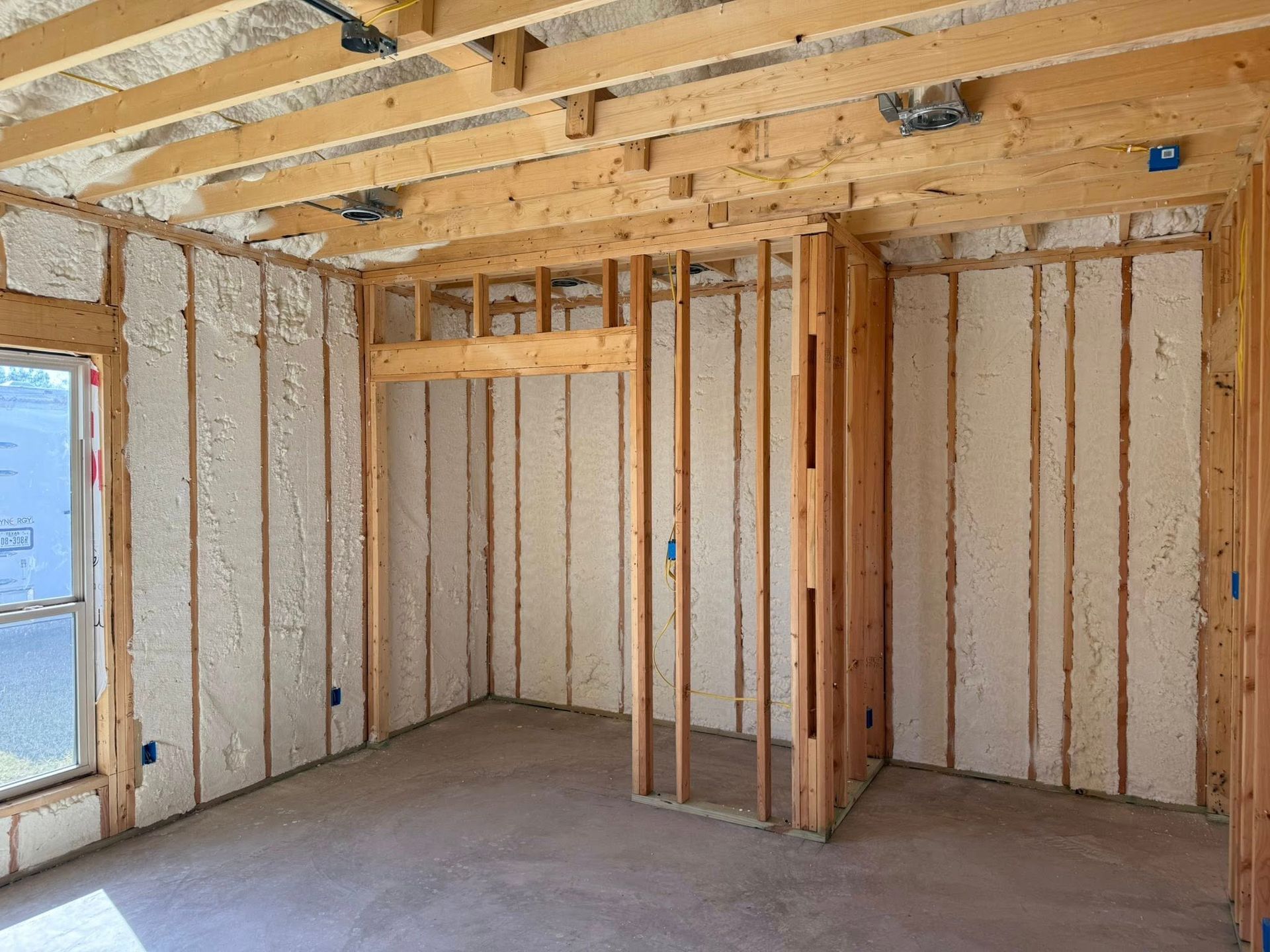 Interior of a room under construction, with exposed wooden framing and spray foam insulation on walls.