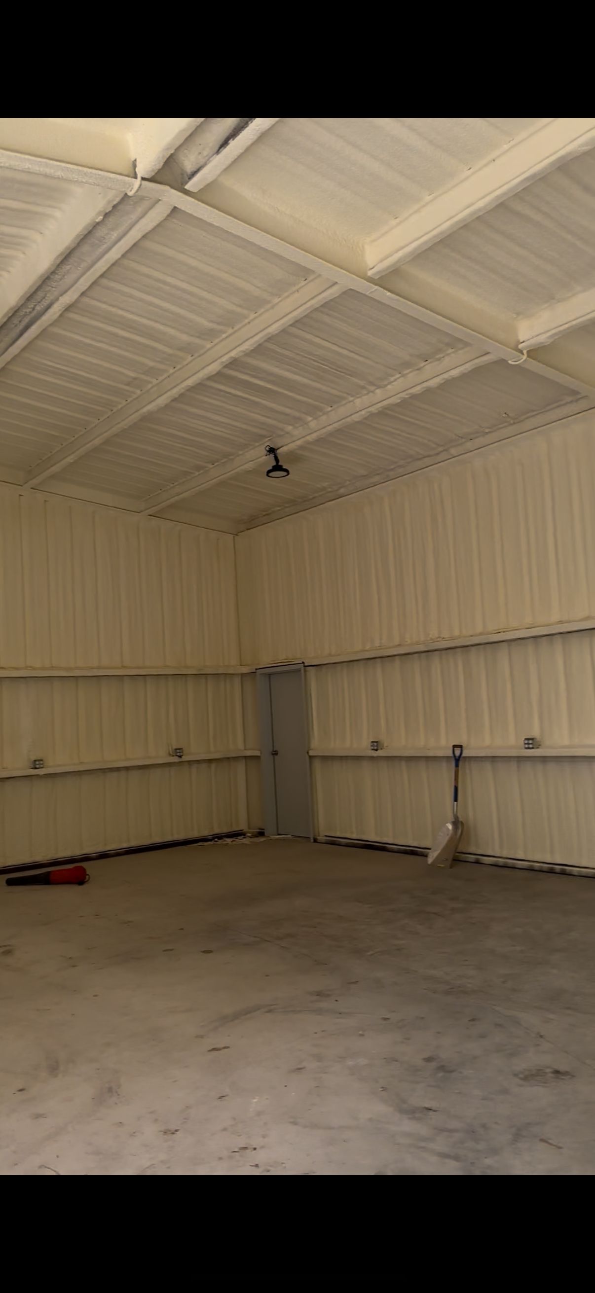 Interior of a building with spray foam insulation. Metal walls and roof. Door and a fan are visible.