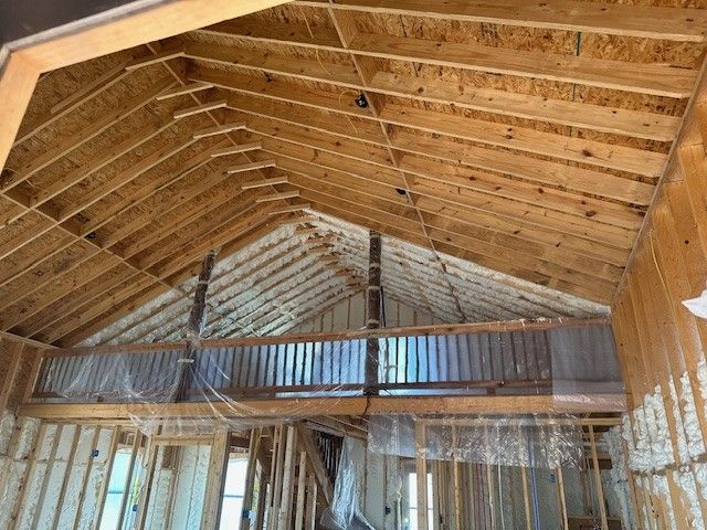 Interior view of a building under construction, featuring exposed wooden rafters, a balcony, and spray foam insulation.