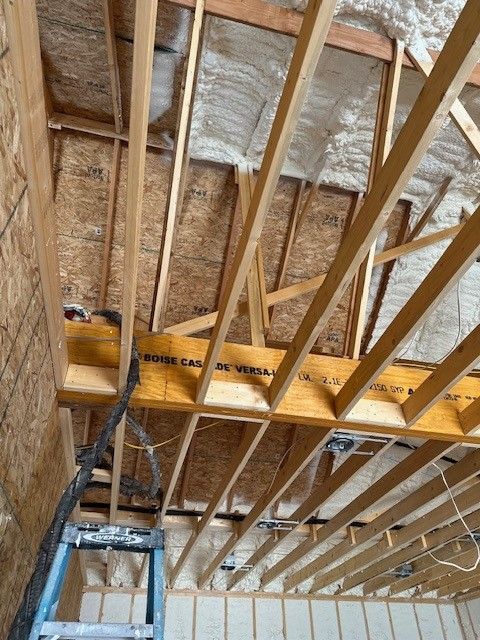 Interior of a wooden roof frame with spray foam insulation. A ladder is in the lower left.
