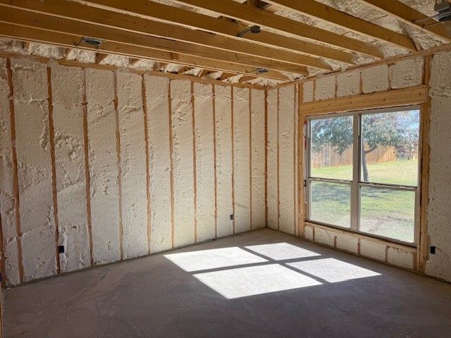 Interior of a room under construction, with exposed wooden framing and spray foam insulation; window with outdoor view.
