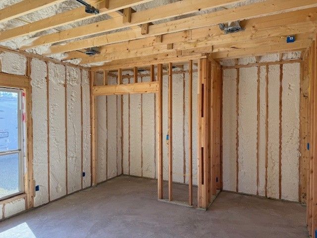 Interior of a room under construction, with exposed wood framing and spray foam insulation.