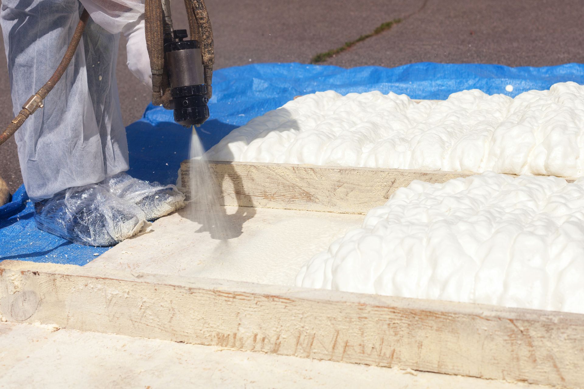 Person spraying white foam insulation onto a surface.