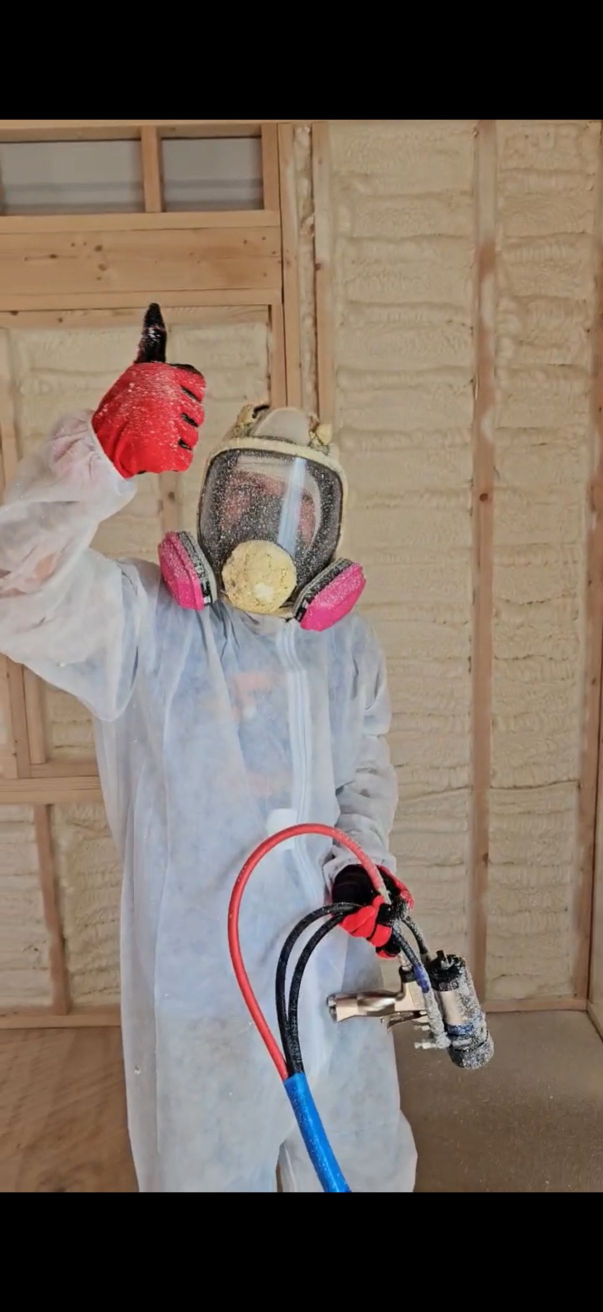 Person in protective suit spraying foam insulation on a wall.