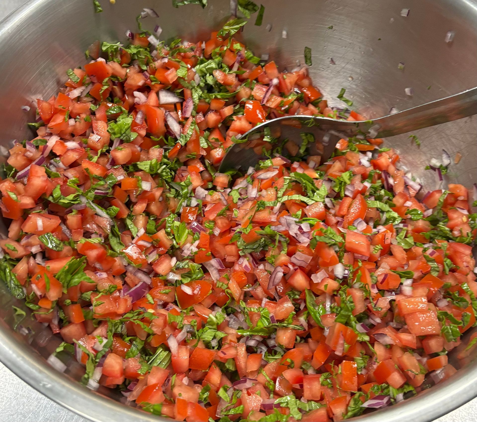 A bowl of chopped tomatoes onions and other vegetables with a spoon in it