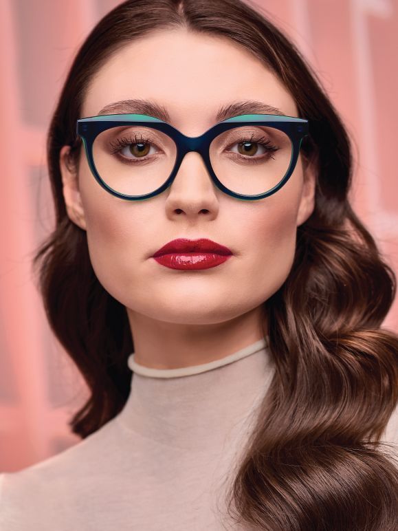 A woman wearing glasses and red lipstick is looking at the camera.