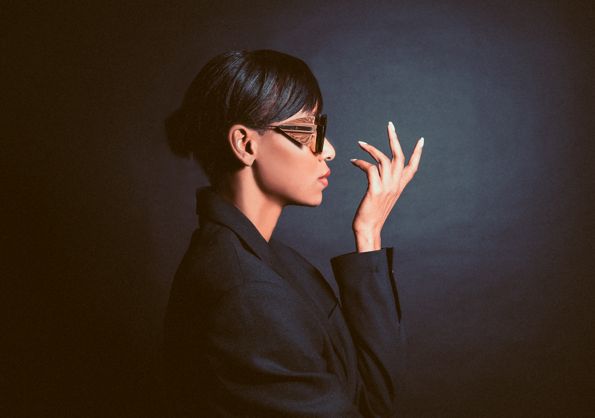 A woman wearing sunglasses and a black jacket is covering her nose with her hand.