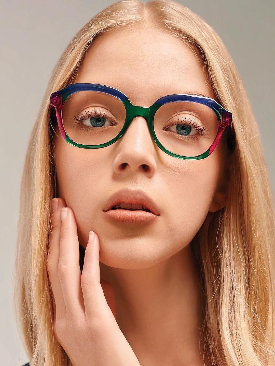 A woman wearing a pair of colorful glasses is touching her face.