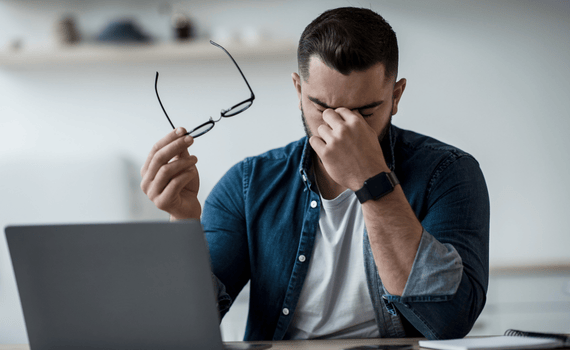 Man with glasses in hand is touching his eyes like he is having pain.