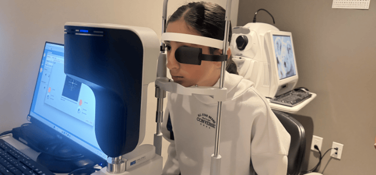 Person wearing protective glasses sits at a vision-testing machine in a clinic