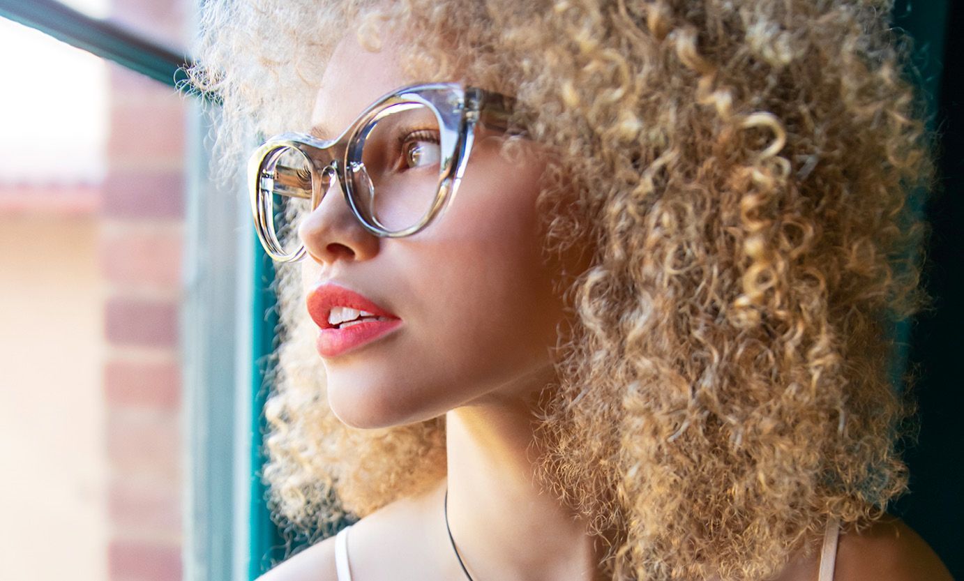 A woman with curly hair and glasses is looking out of a window.