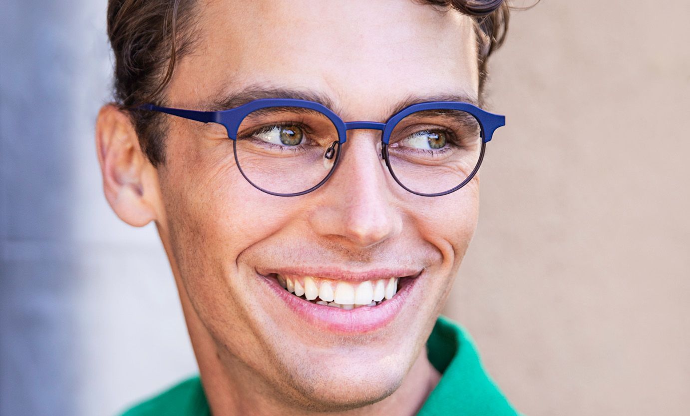 A man wearing glasses and a green shirt is smiling.