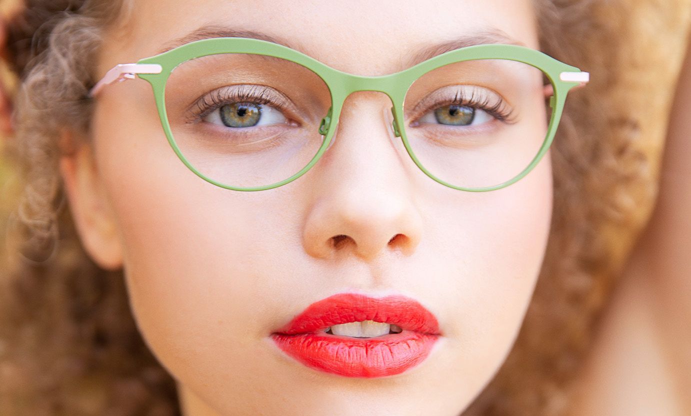 A close up of a woman wearing green glasses and red lipstick.