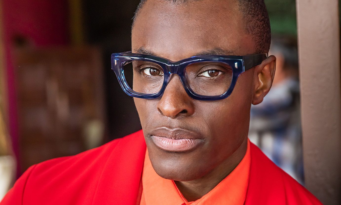 A man wearing glasses and a red jacket is looking at the camera.