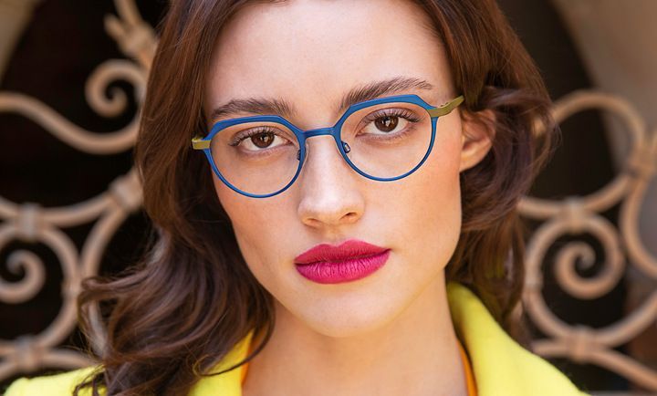 A woman wearing titanium glasses and a yellow jacket is looking at the camera.