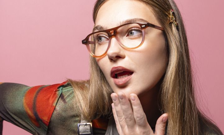 A woman wearing glasses is covering her mouth with her hand.