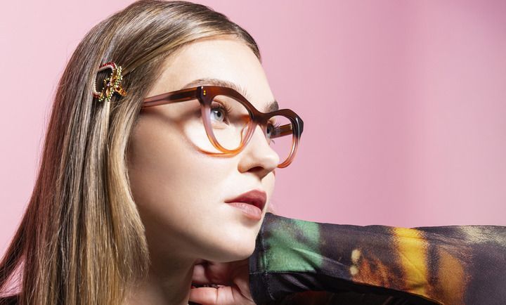 A close up of a woman wearing glasses on a pink background.
