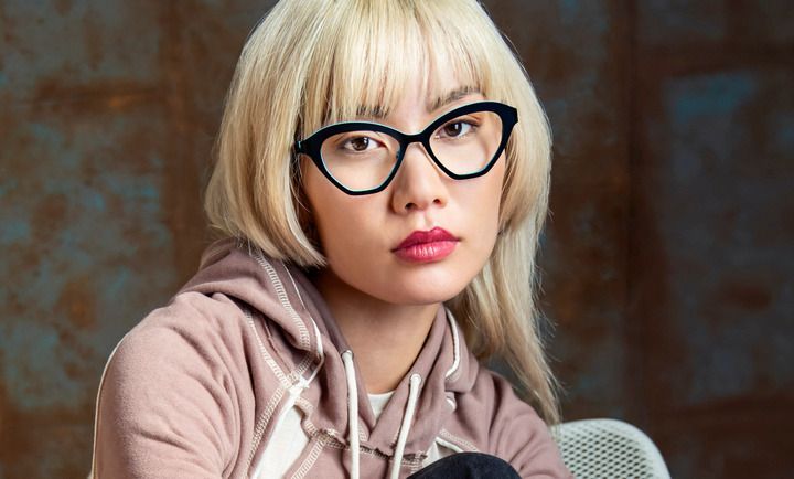 A woman wearing glasses and a hoodie is sitting in a chair.