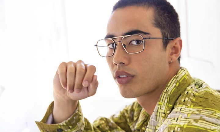 A young man wearing glasses and a green shirt is sitting at a table.