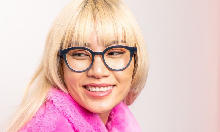 A woman wearing glasses and a pink sweater is smiling.