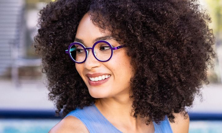 A woman with curly hair is wearing glasses and smiling.