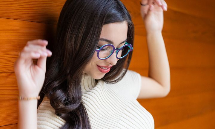 A woman wearing glasses is leaning against a wooden wall.