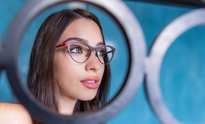 A woman wearing glasses is looking at herself in a mirror.