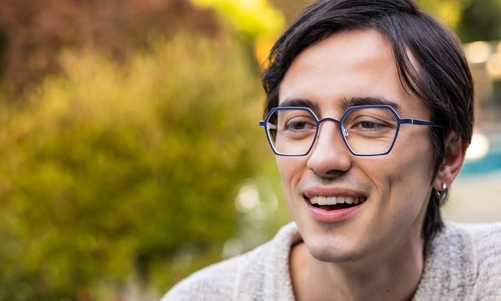 A young man wearing glasses is smiling and looking to the side.