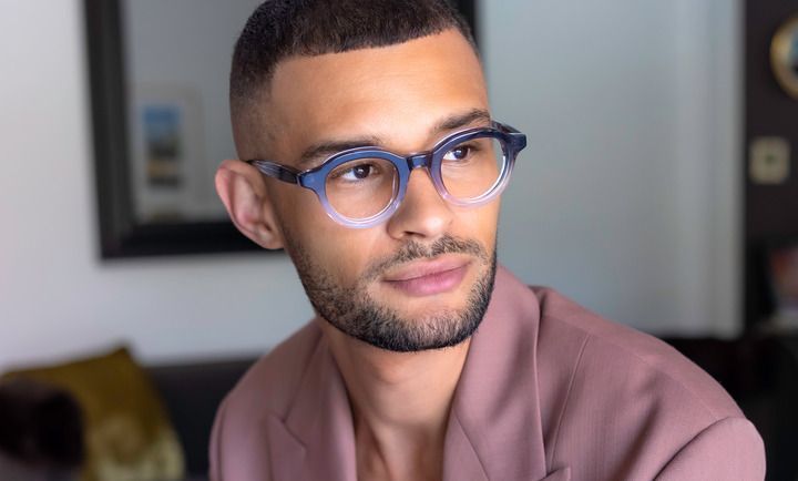 A man wearing glasses and a pink jacket is sitting on a couch.