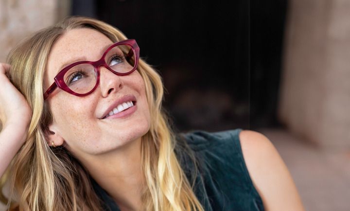 A woman wearing glasses is smiling and looking up.