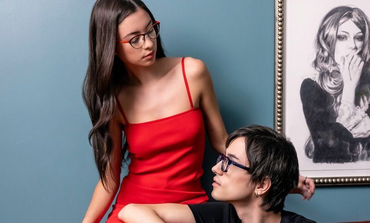 A woman in a red dress is standing next to a man wearing glasses.