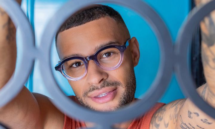 A man wearing glasses is taking a selfie with a ring light.