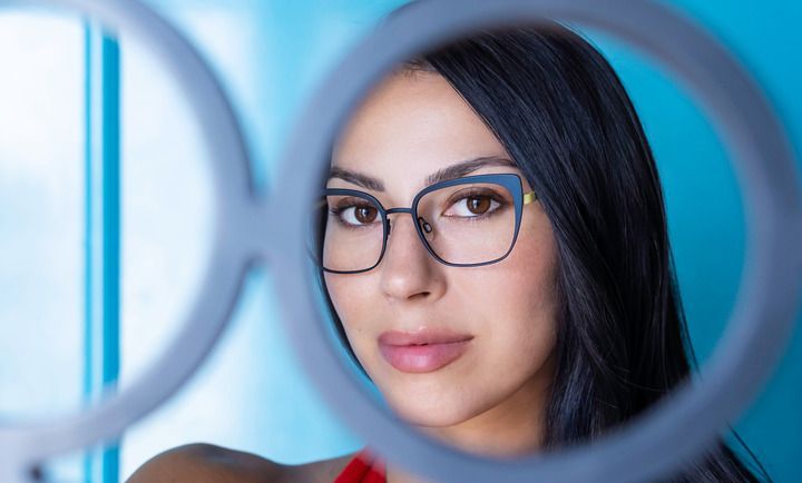 A woman wearing glasses is looking through a ring light.