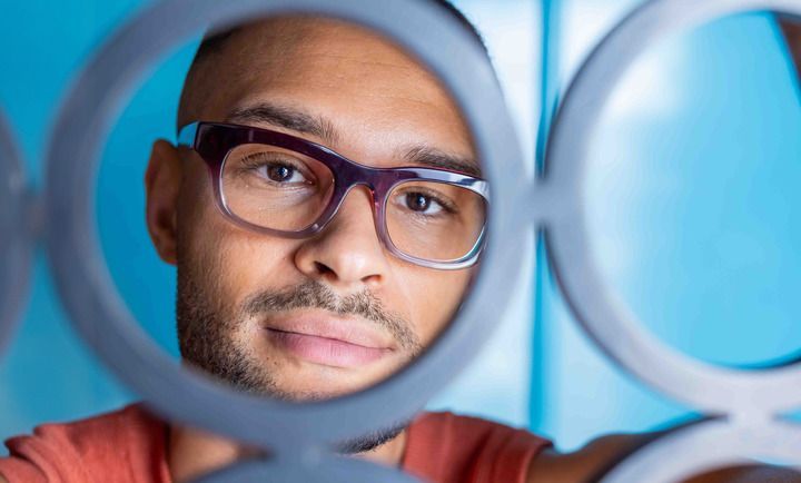 A man wearing glasses is looking at himself in a mirror.