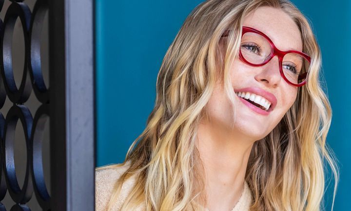 A woman wearing red glasses is smiling and looking up.