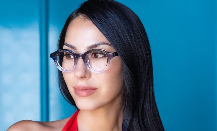 A woman wearing glasses is standing in front of a blue wall.