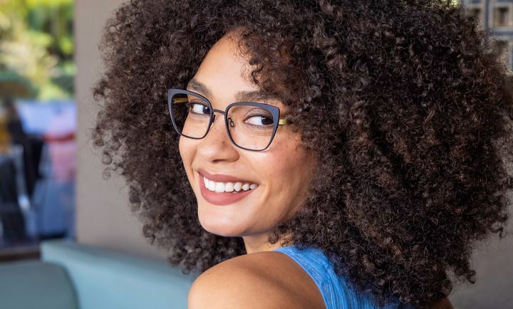 A woman with curly hair is wearing glasses and smiling.