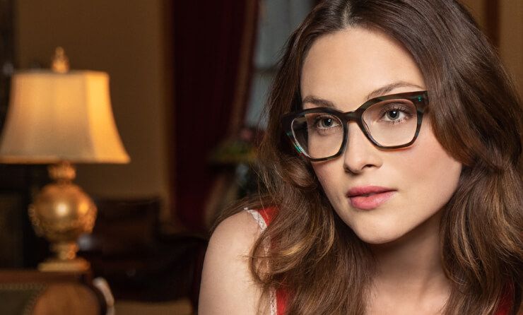 A woman wearing glasses is sitting in front of a lamp.