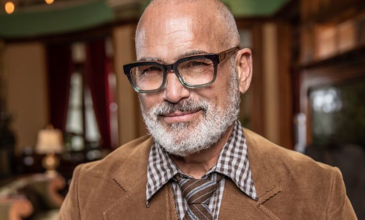 A man with a beard and glasses is wearing a brown jacket and tie.