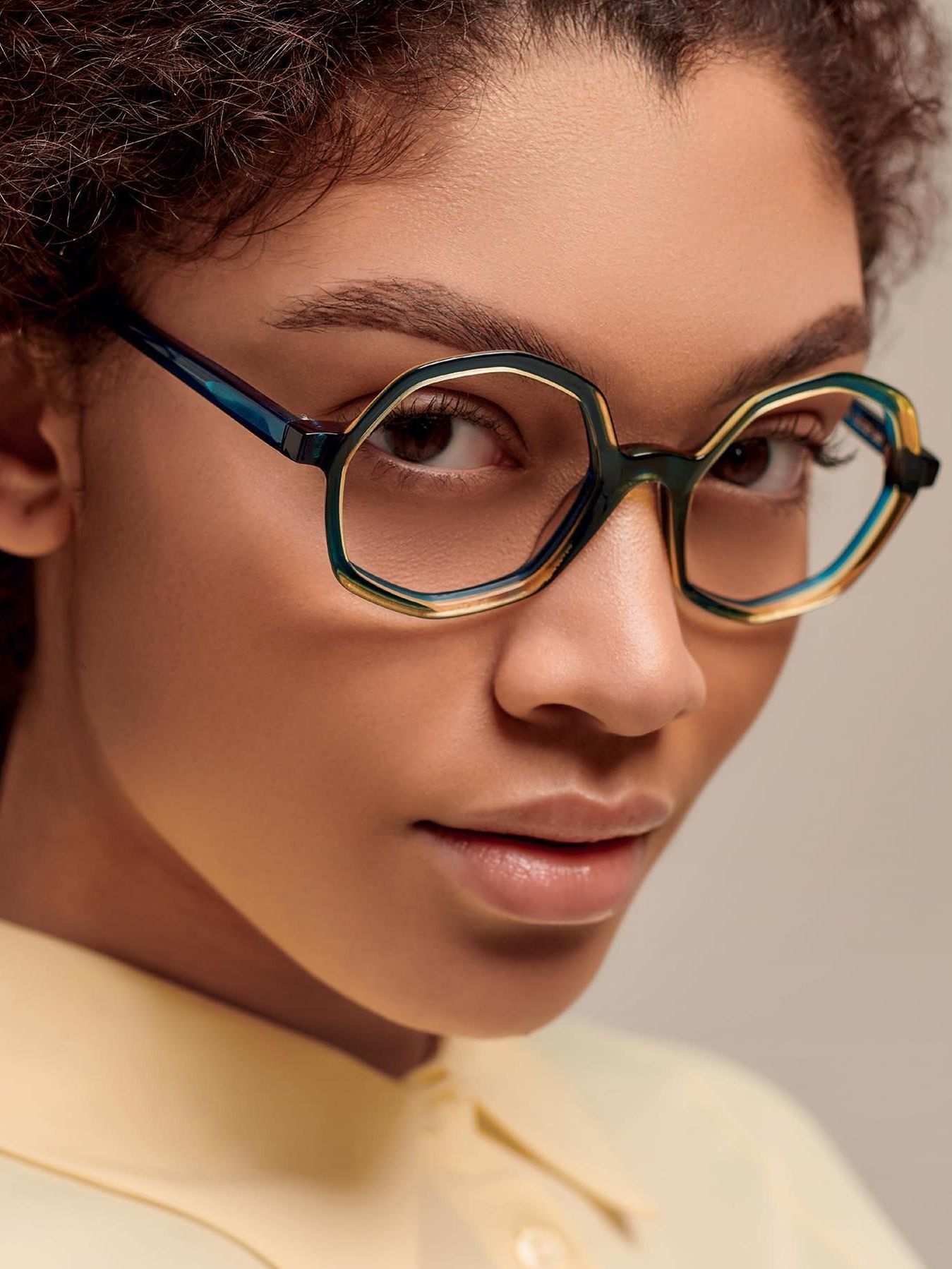 A close up of a woman wearing glasses and a yellow shirt