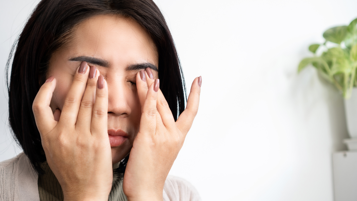 A woman is rubbing her eyes with her hands.