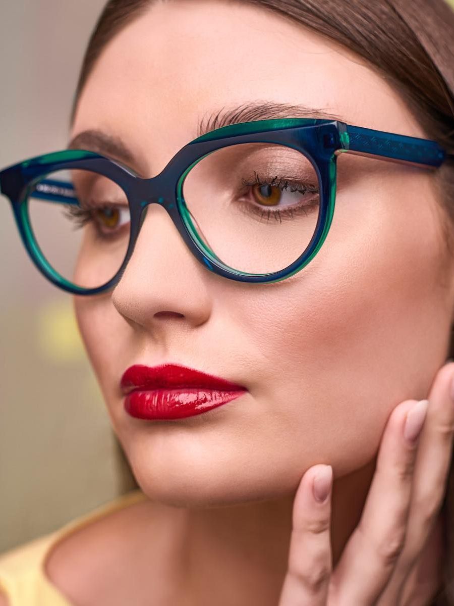 A woman wearing glasses and red lipstick is touching her face.